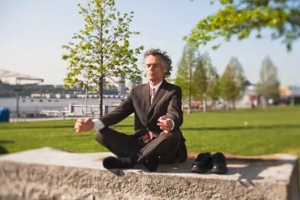 Successful trader practicing work-life balance through meditation outdoors, wearing a business suit.